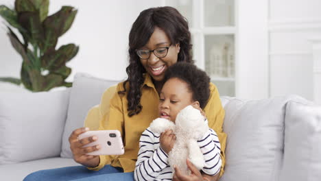 Schöne-Junge-Mutter-Sitzt-Mit-Süßer-Kleiner-Tochter-Auf-Der-Couch-Und-Hat-Online-Einen-Videochat-Auf-Dem-Smartphone