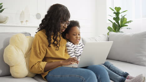 Mother-In-Glasses-Showing-Something-To-Small-Cute-Daughter-On-Laptop