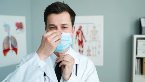 Young-Male-Doctor-Talking-To-Camera-And-Teaching-To-Wear-Medical-Mask-In-Cabinet