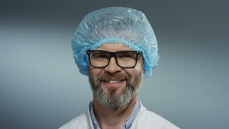 Retrato-Del-Apuesto-Médico-De-Pelo-Gris-Con-Gafas,-Sombrero-Azul-Y-Barba-Sonriendo-Alegremente-A-La-Cámara