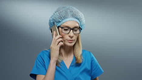 Young-Asan-Busy-Blonde-Woman-Doctor-In-Blue-Costume,-Hat-And-Glasses-Talking-On-The-Phone-Emotionally