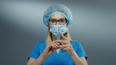 Close-Up-Of-The-Young-Blonde-Woman-Doctor-In-Hat,-Glasses-And-Mouth-Mask-Holding-A-Syringe-With-A-Needle