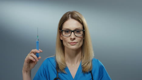 Portrait-Of-The-Young-Blond-Beautiful-Woman-Physician-In-The-Glasses-Holding-A-Syringe-With-A-Needle-And-Smiling-Cherfully