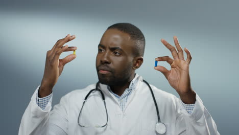 Young-Male-Physician-Holding-Two-Pills-In-Hands,-One-Yellow-And-One-Blue,-While-Comparing-Them-And-Studying-Carefully