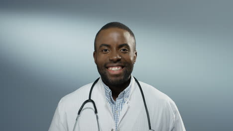 Close-Up-Of-The-Young-Happy-Male-Doctor-Or-Intern-Smiling-Cheerfully-To-The-Camera-On-The-Gray-Wall-Background