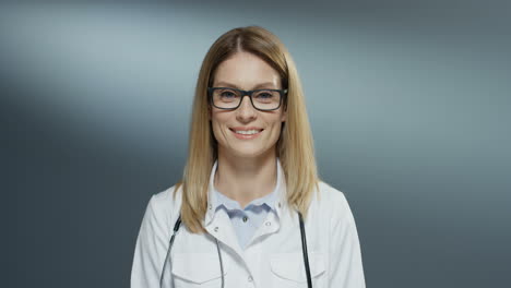 Porträtaufnahme-Der-Jungen-Schönen-Blonden-Ärztin-Mit-Brille-Und-Weißem-Arztkittel,-Die-Glücklich-In-Die-Kamera-Lächelt