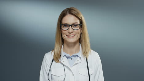 Close-Up-Of-The-Young-Charming-Blond-Female-Physician-In-Glasses-And-White-Medical-Clothes-Smiling-Cheerfully-To-The-Camera