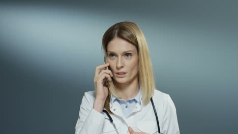Good-Looking-Young-Female-Physician-In-White-Medical-Gown-Speaking-On-The-Mobile-Phone-Like-Solving-Some-Problems-And-Explaining-Issues