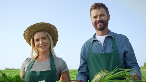 Portrait-Shot-Of-The-Good-Looking-And-Happy-Woman-And-Man-Farmers-Smiling-To-The-Camera-On-The-Field-With-Harvested-Vegetables-In-Hands