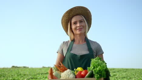 Portrait-Shot-Of-The-Blond-Young-Good-Looking-Woman-Farmer-In-A-Hat-And-With-A-Box-Full-Of-The-Harvested-Vegetables-In-Field