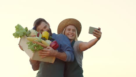 Paar-Der-Jungen-Gutaussehenden-Und-Glücklichen-Bauern-Lächeln-Und-Posieren-Vor-Der-Smartphone-kamera,-Während-Sie-Selfie-fotos-Mit-Geerntetem-Gemüse-In-Den-Händen-Machen