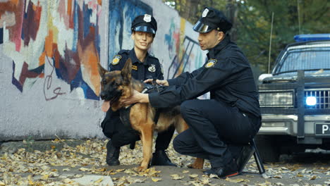 Fröhliches-Paar-Polizist-Und-Polizistin,-Die-Auf-Der-Straße-Sitzen-Und-Schäferhund-Streicheln