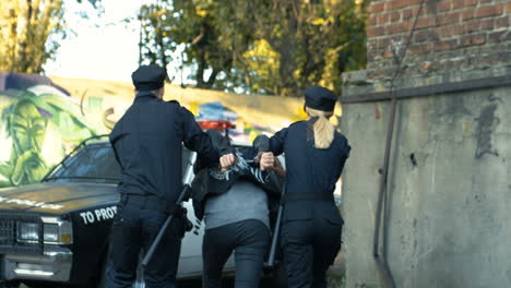 Back-View-On-Couple-Of-Police-Officers-Escorting-Female-Criminal-To-The-Car