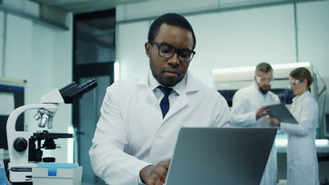 Young-Handsome-Man-Scientist-Doing-Some-Investigation-At-The-Laptop-Computer-And-Analysis-While-Looking-In-The-Microscope-In-The-Laboratory