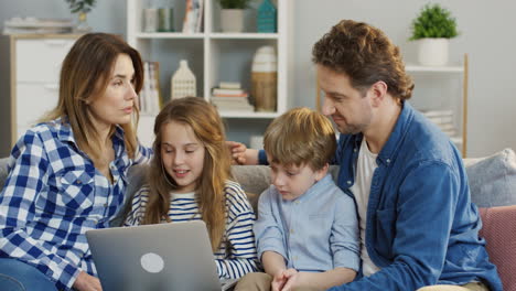 Young-Nice-Family-With-Kids-Sitting-At-Home-On-The-Couch-And-Watching-Something-On-The-Laptop-Computer
