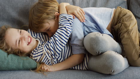 Two-Small-Funny-Children,-Brother-And-Sister,-Having-Fun-On-The-Sofa-In-The-Cozy-Living-Room,-Hugging-And-Laughing
