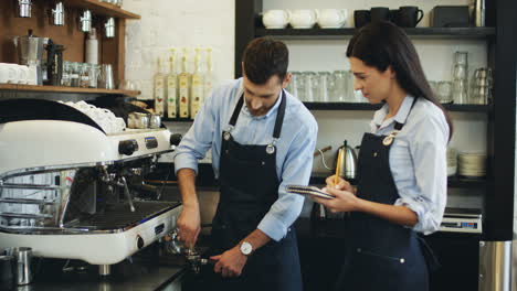 Waiter-Making-Coffee-At-The-Coffee-Machine-While-Demonstrating-This-And-Teaching-Young-New-Waitress-Which-Noting-In-The-Notebook