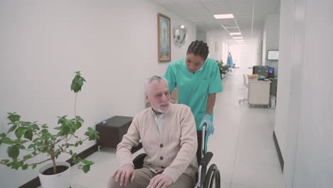 An-Old-Man-With-A-Beard-And-Gray-Hair-Is-Dragged-By-A-Young-Female-Nurse-In-His-Wheelchair
