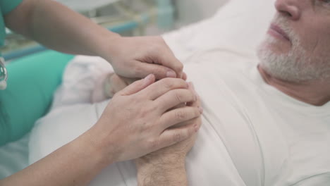 Detail-Of-A-Nurse's-Hands-Grasping-And-Comforting-The-Hands-Of-A-Sick-Patient-On-Hospital-Bed