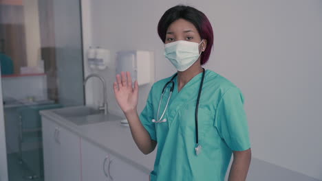 Young-Female-Doctor-With-A-Facemask-Says-Hello-To-The-Camera