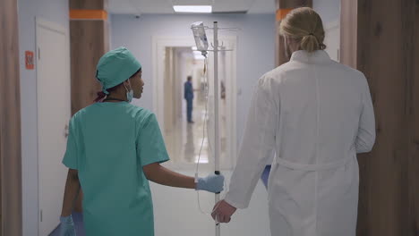A-Cute-Young-American-Nurse-And-A-Young-Doctor-With-Long,-Blond-Hair-Walk-Together-Down-The-Hospital-Corridor