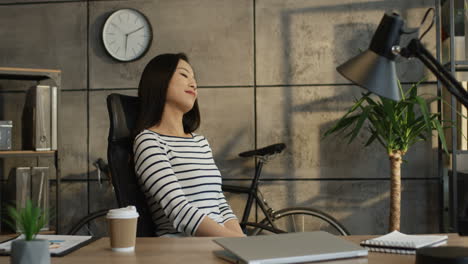 Young-Woman-Sitting-In-The-Office-At-Her-Working-Place-And-Resting-While-Dreaming-With-A-Smile-On-Her-Face