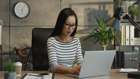 Young-Female-Office-Worker-In-Glasses-Working-On-The-Laptop-Computer,-Tapping-And-Typing-On-The-Keyboard-While-Texting