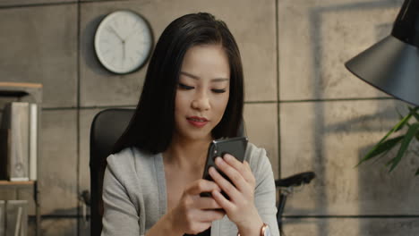 Portrait-Of-The-Young-Pretty-Woman-Office-Manager-Reading-Something-On-The-Smartphone-Screen-And-Texting-On-It,-Then-Smiling-To-The-Camera