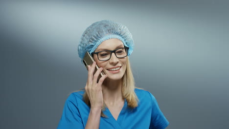 Attraktive-Junge-Sanitäterin-In-Blauem-Kostüm,-Hut-Und-Brille,-Die-Fröhlich-Am-Telefon-Spricht-Und-Lächelt