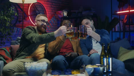 Multiethnic-Cheerful-Guys-Sitting-On-The-Sofa-With-Beer-And-Snacks,-Talking-And-Watching-Tv-With-Sport-Channel