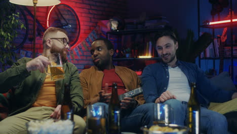 Mixed-Races-Good-Looking-Happy-Men-Talking-With-Beer-And-Snacks-Watching-Tv-Together-In-The-Evening-At-Home