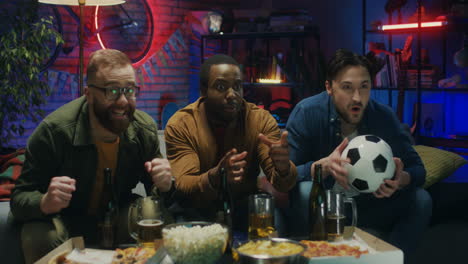 Three-Multiethnic-Friendly-And-Cheerful-Young-Men-Celebrating-Victory-Of-Their-Football-Team-In-The-Championship-In-The-Dark-Living-Room-With-Snacks-And-Beer