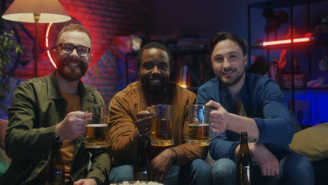 Portrait-Shot-Of-The-Three-Mixed-Races-Young-Handsome-Guys-Friends-Smiling-To-The-Camera-With-Beer-In-Hands-In-The-Dark-Living-Room