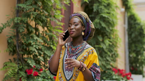 Pretty-Young-Woman-In-The-Traditional-Clothes-Talking-On-The-Phone-Joyfully-In-The-Nice-Courtyad-With-Flowers