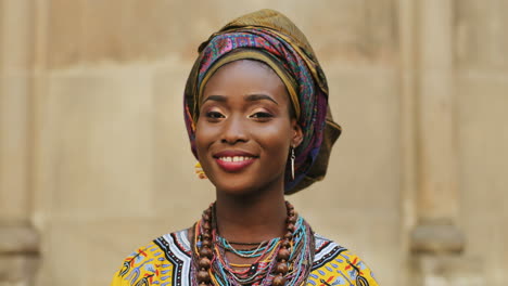 Close-Up-Of-The-Young-Attractive-Woman-In-The-Traditional-Clothes-And-With-Scarf-Over-Her-Head-Looking-Straight-To-The-Camera-And-Smiling-On-The-Wall-Background