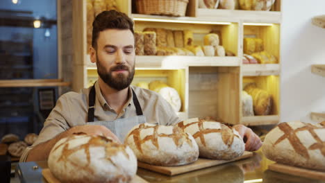 Close-Up-Of-The-Young-Baker-Man-Standing-Near-The-Counter-In-The-Bakery-Shop-And-Smelling-Just-Baked-Bread