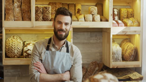 Portrait-Of-The-Young-Male-Bread-Seller-In-The-Apron-Looking-At-The-Side-And-Then-Smiling-To-The-Camera-In-The-Bakery-Shop