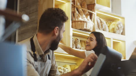 Close-Up-Of-Young-Male-And-Female-Bread-Vendors-Selling-Baguettes-To-The-Buyer-At-The-Counter-In-The-Bakery-Shop