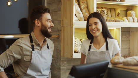 Male-And-Female-Bakery-Vendors-Standing-At-The-Counter-And-Talking-Joyfully