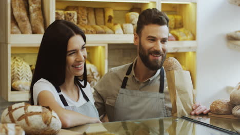 Ein-Gutaussehender-Männlicher-Verkäufer-In-Der-Bäckerei,-Der-Baguettes-Verkauft,-Während-Seine-Mitarbeiterin-In-Der-Nähe-Steht-Und-Lächelt