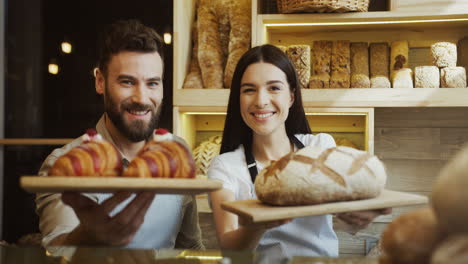 Porträt-Der-Beiden-Gut-Aussehenden-Jungen-Lächelnden-Bäcker-Und-Bäckerinnen,-Die-Mit-Einem-Brot-Und-Croissants-An-Der-Theke-Posieren