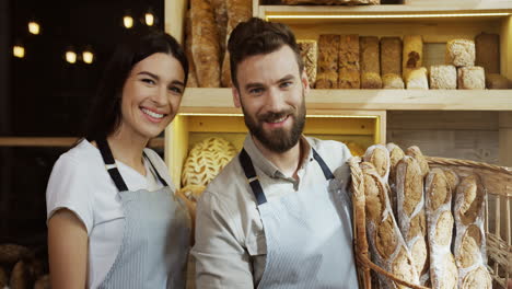 Portrait-Shot-Of-The-Attractive-Young-Male-And-Female-Bakers-In-Aprons-Smiling-While-Posing-With-Baguettes-In-The-Basket-In-The-Bakery-Shop
