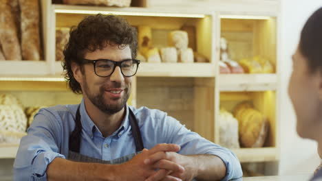 Close-Up-Of-The-Handsome-Male-Vendor-In-The-Bakery-Shop-Talking-With-The-Young-Woman-Who-Buying-Bread