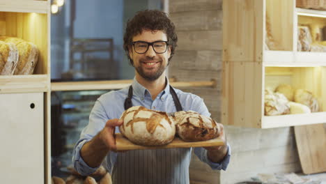 Portrait-Shot-Of-The-Attractive-Young-Man,-Bakery-Vendor,-Holding-A-Tray-With-Fresh-Bread-And-Looking-At-The-Camera-With-A-Smile