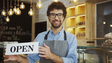Male-Smiled-Bakery-Vendor-Posing-With-A-Signboard-Open-And-Smiling-In-The-Shop