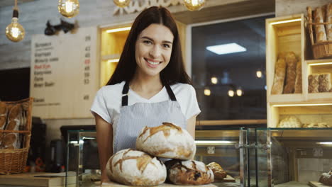 Portrait-Of-The-Young-Woman-Baker-Looking-At-The-Camera-While-Holding-A-Tray-With-Bread-In-The-Shop