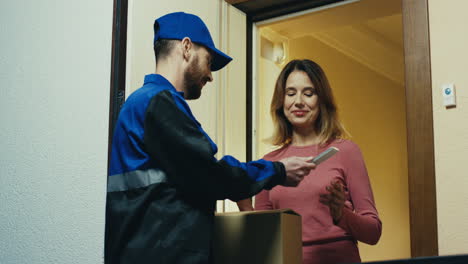 Male-Worker-Of-The-Shipping-Company-In-The-Blue-Costume-Standing-At-The-Door-And-Handing-A-Box-To-The-Smiled-Woman