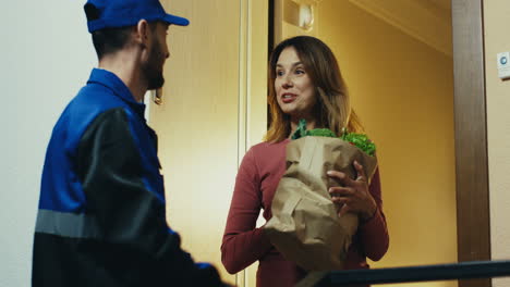 Mann-In-Der-Blauen-Uniform-Von-Der-Supermarktlieferung,-Der-Der-Attraktiven-Frau-An-Ihrer-Tür-Ein-Paket-Mit-Gemüse-überreicht