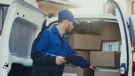 Postbote-In-Blauer-Uniform-Steht-Am-Weißen-Lieferwagen-Und-Kontrolliert-Kartonpakete,-Schreibt-Dann-Infos-Auf