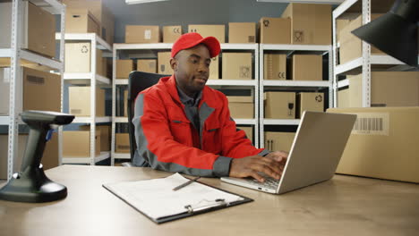 Junger-Mann-In-Uniform-Sitzt-Am-Tisch-Und-Tippt-Auf-Laptop-Computer,-Während-Er-Den-Briefkasten-Im-Postamt-Registriert